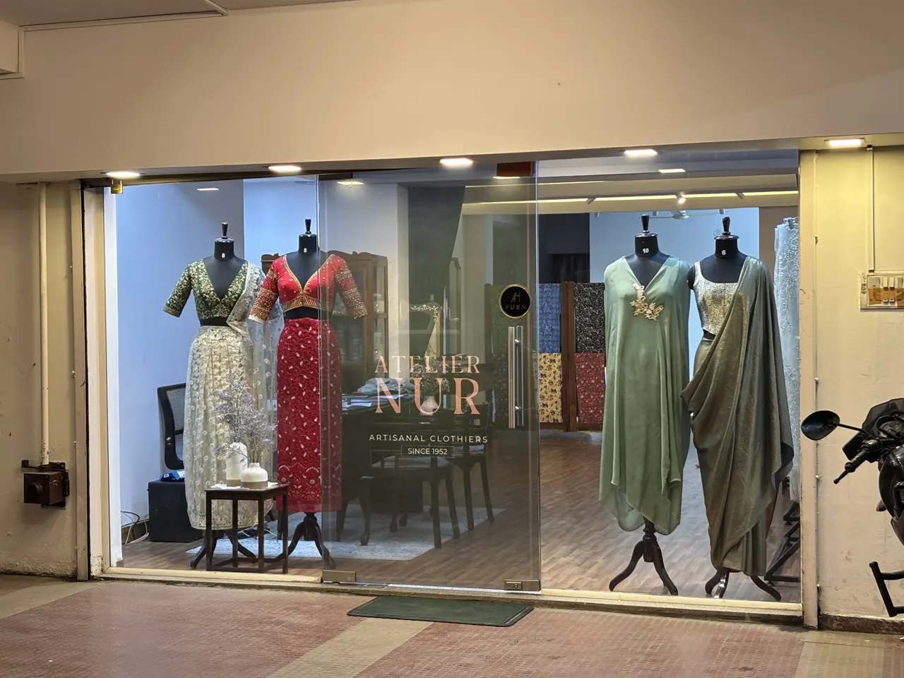 Glass shopfront of Atelier Nur with garments displayed on dress forms.