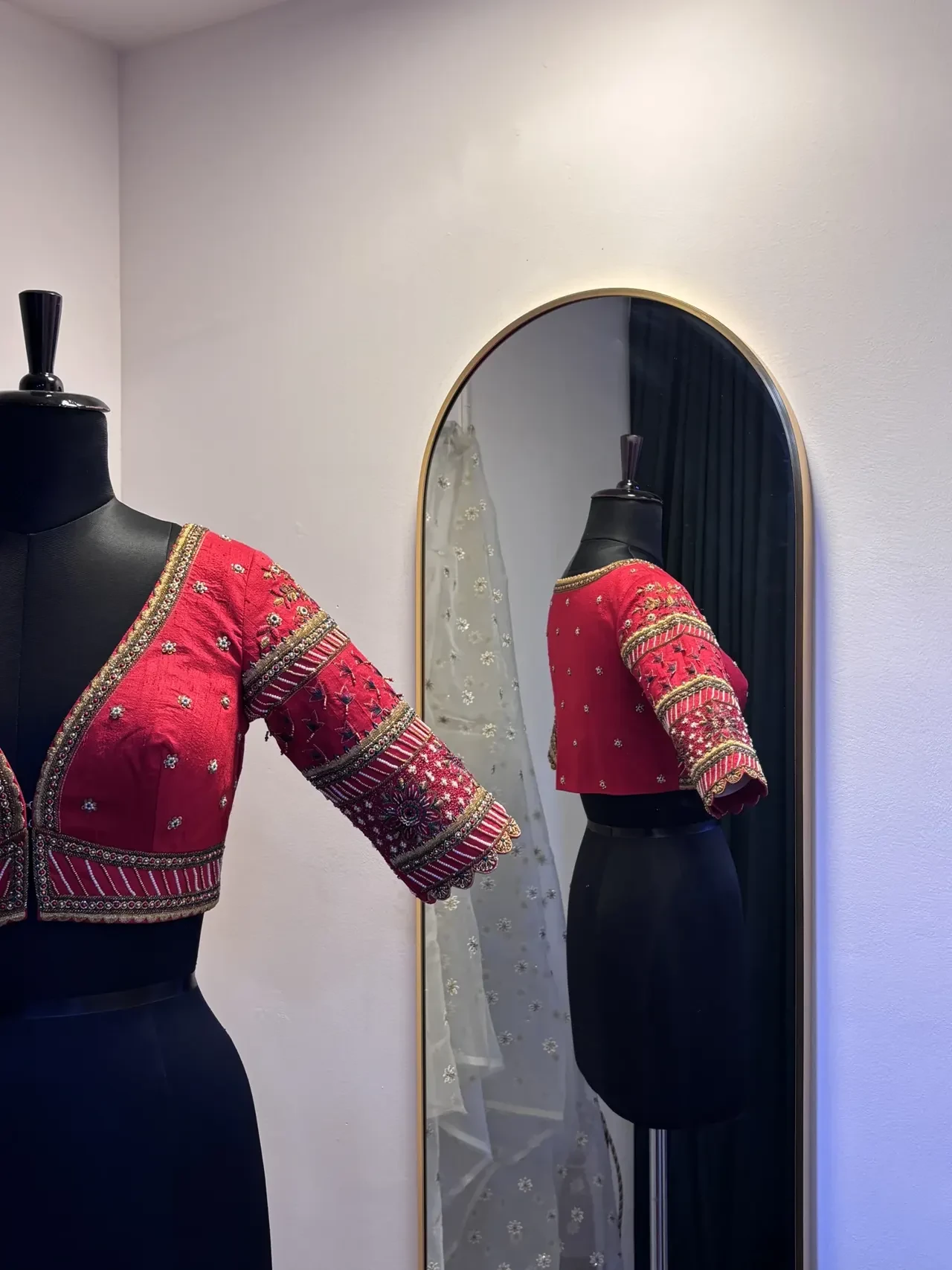 Red embroidered blouse on a dress form beside an arched mirror.