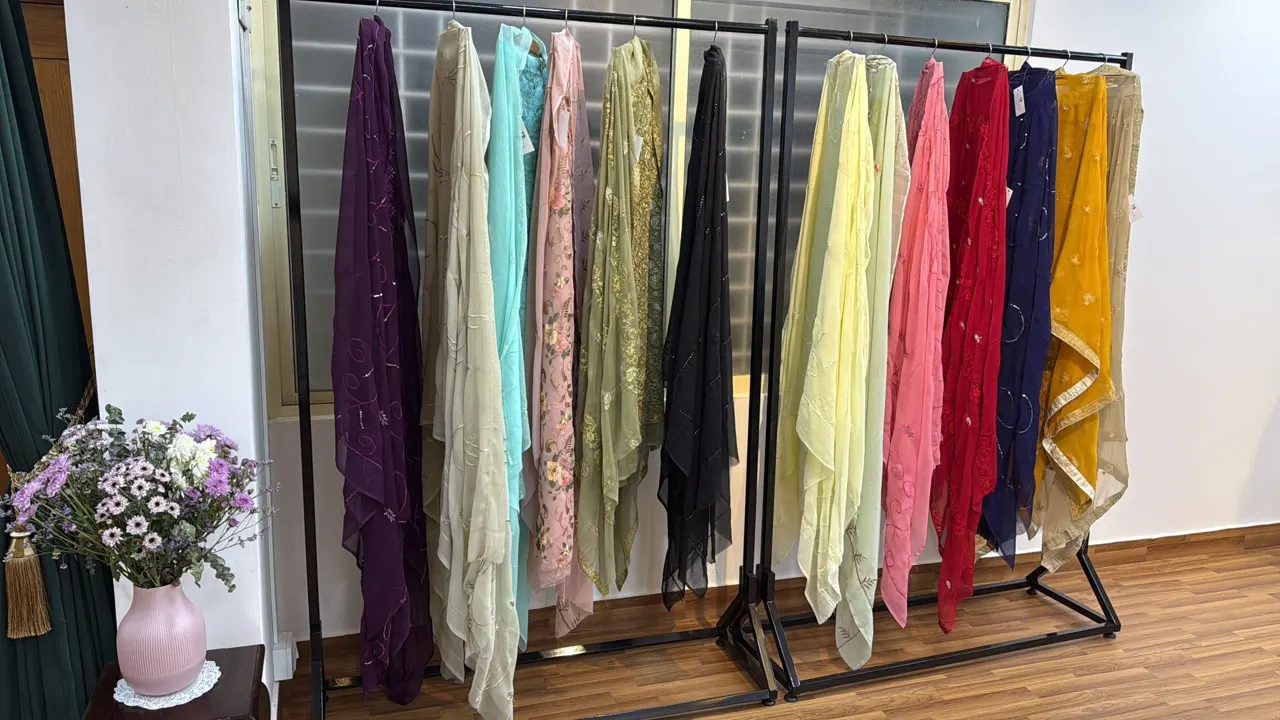 A rail of fabrics in soft colours beside a vase of flowers.