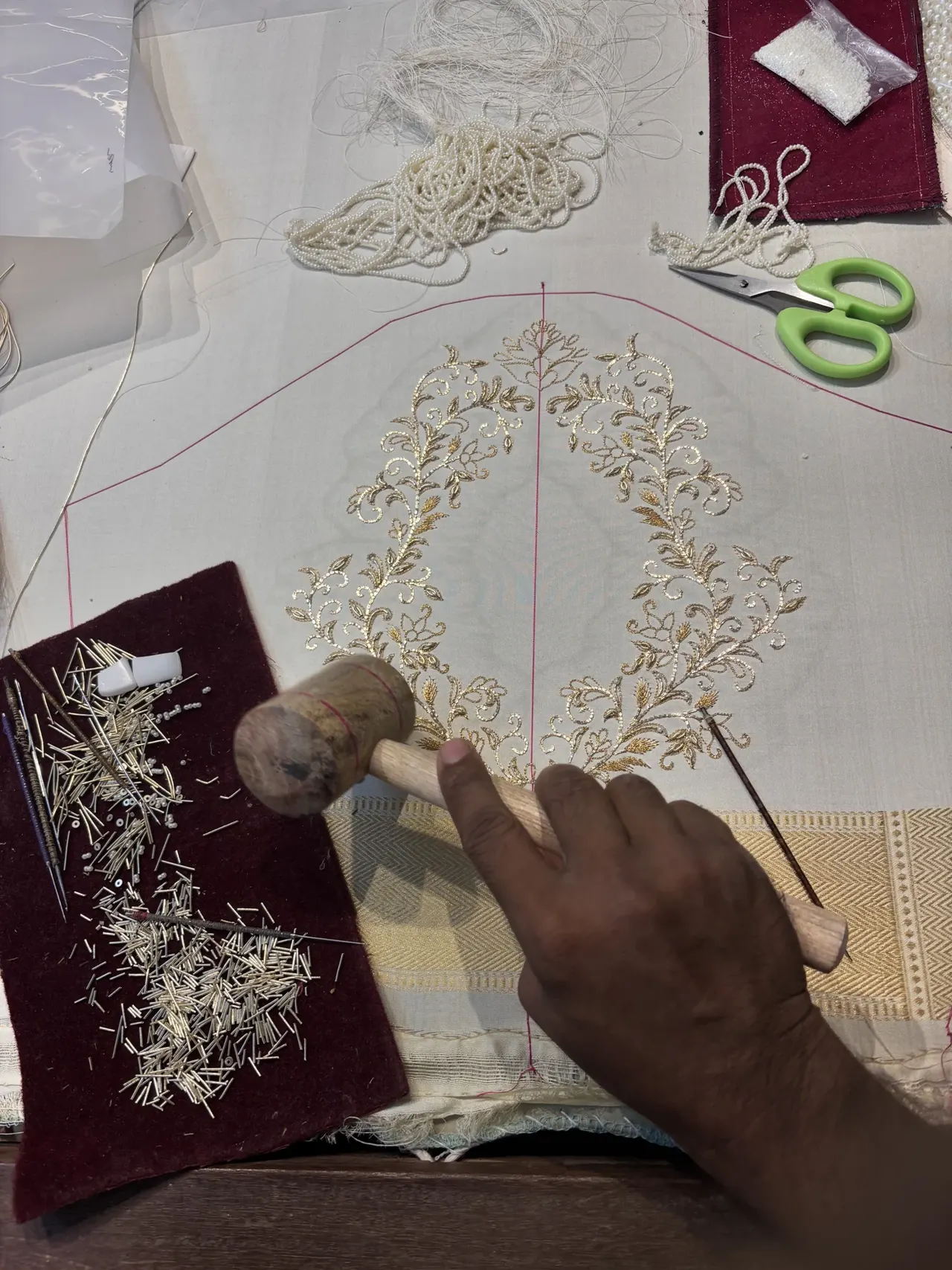 Hands working gold embroidery onto fabric stretched on a frame.