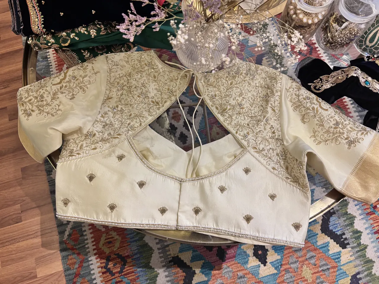 Ivory blouse with gold embroidery laid out on a patterned rug.