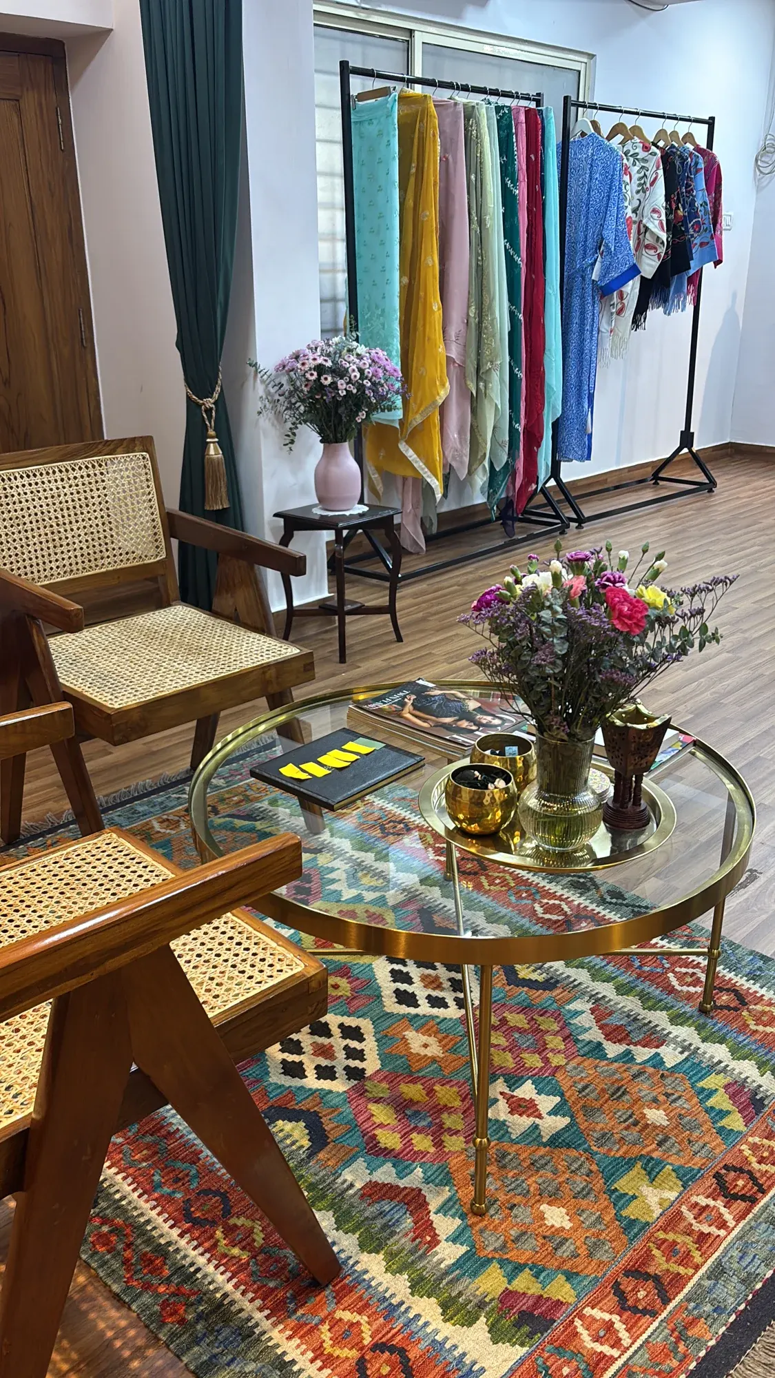 Cane chairs, a glass table with flowers and a rail of fabrics at Atelier Nur.